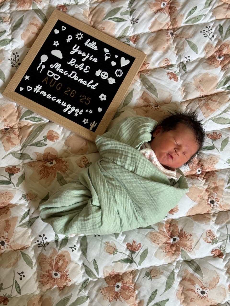 Baby Yoojin swaddled lying next to an announcement board reading “Hello, Yoojin Rae MacDonald, Aug 26 ‘25, #macnugget”