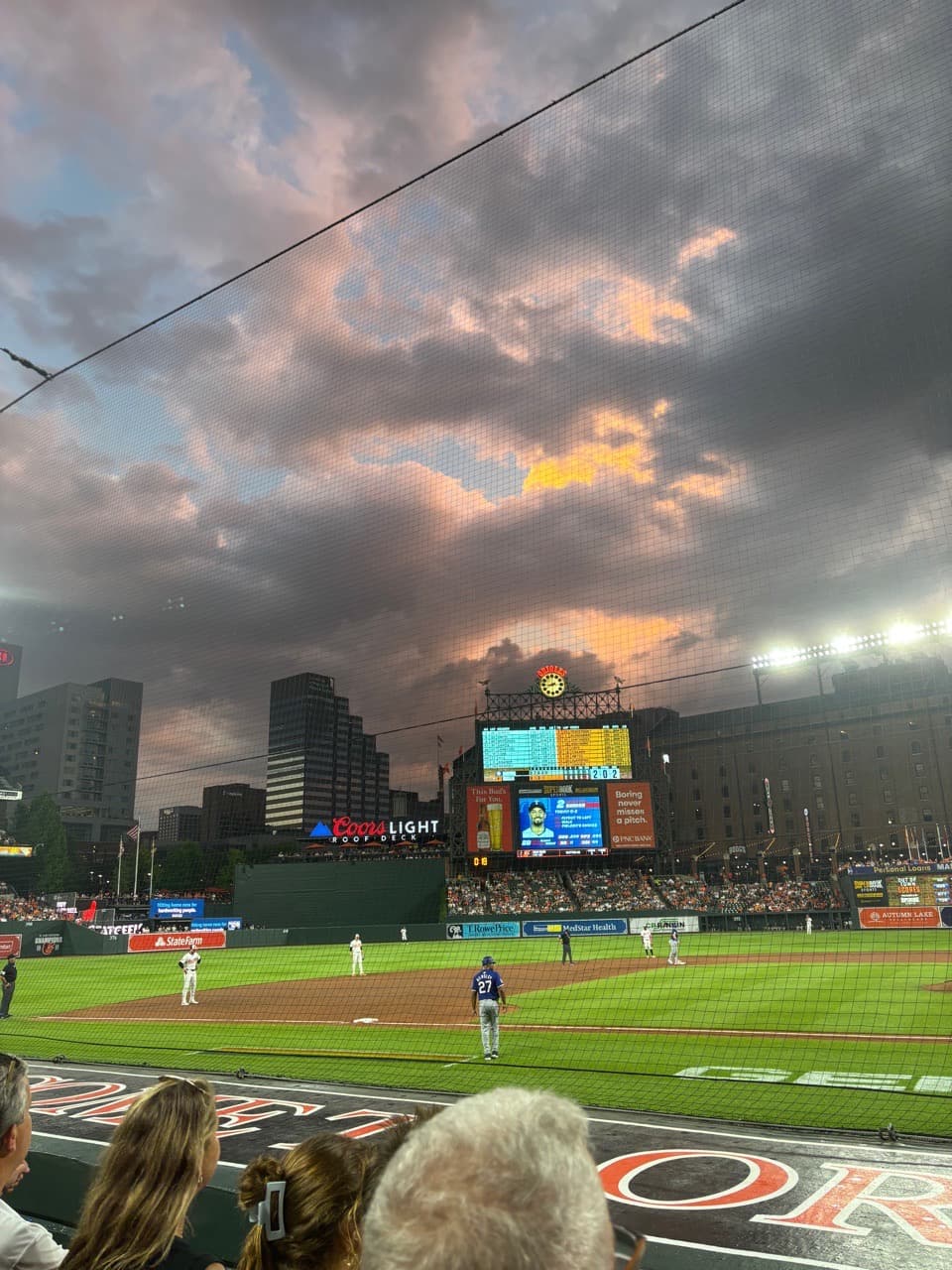 Orange skies above Camden Yards. Orioles players stand ready on defense waiting for the pitch.